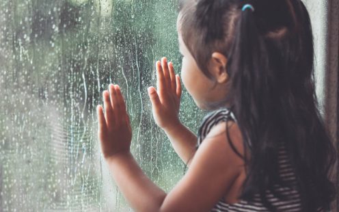 Sad asian little girl looking outside through the window in the rainy day in vintage color tone