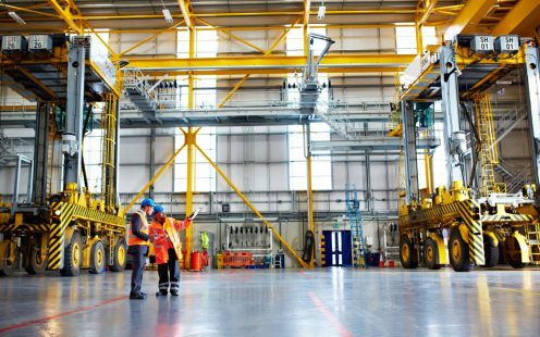 Shot of two warehouse workers talking together over a clipboard inside of a large warehouse