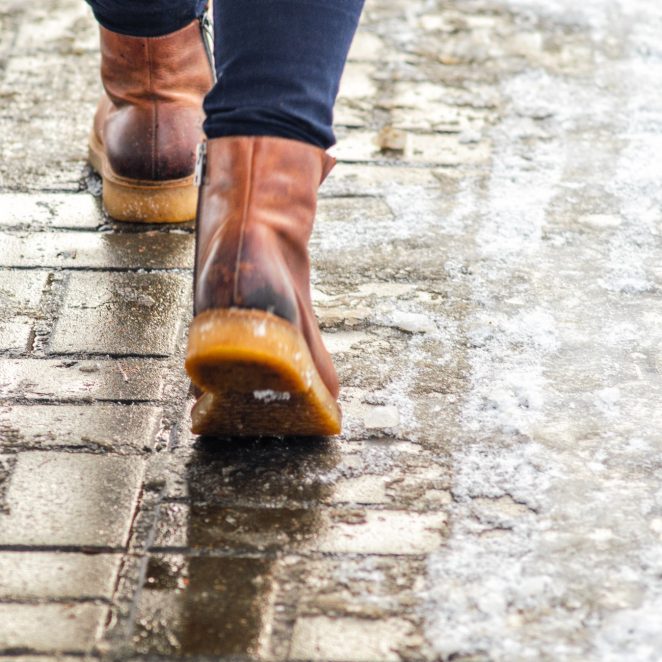 Walk on wet melted ice pavement. Back view on the feet of a man walking along the icy pavement. Pair of shoe on icy road in winter. Abstract empty blank winter weather background